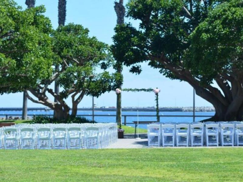 Outdoor wedding setup with chairs facing a floral arch by the water.